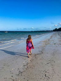 Full length rear view of woman walking on shore at beach against sky