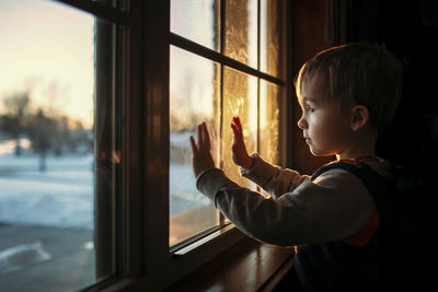 Boy looking through window while standing in darkroom at home