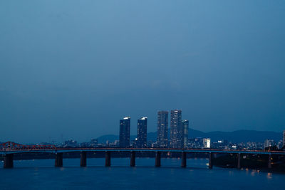 Illuminated bridge over river against clear sky