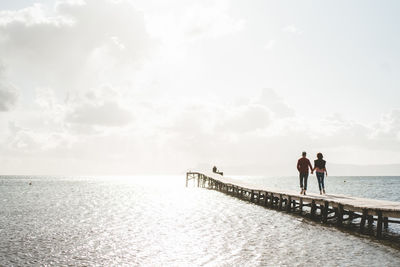 Mature couple holding hands walking on jetty over sea