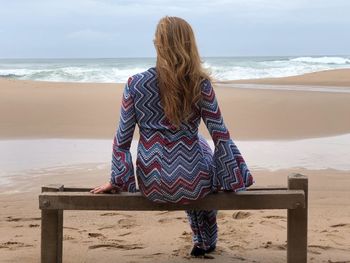 Rear view of woman sitting at beach against sky