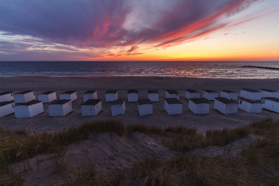 Huts at beach against cloudy sky during sunset