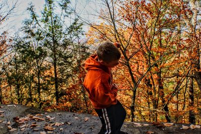 Full length of boy standing by tree in forest during autumn