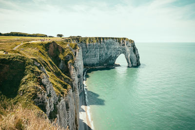 Scenic view of cliff by sea against cloudy sky