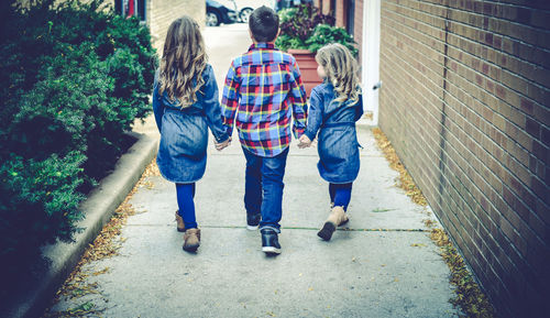 Rear view of friends holding hands while walking on footpath