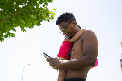 Father holding daughter in his arms and typing on his mobile phone