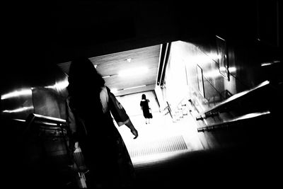 Silhouette people walking on illuminated staircase in city