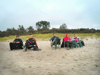 Friends sitting on field against sky