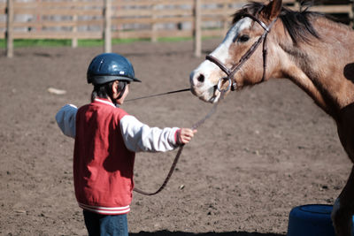 Boy holding horse with bridle at ranch