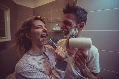 Smiling young woman with man holding toothbrush in bathroom at home