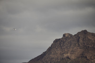 Plane flying in gray cloudy sky above rocky mountain peak