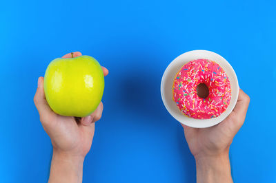 Green apple and pink donut in male hands, the concept of choosing health and unhealthy food on a