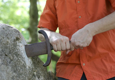 Midsection of man holding sword in rock