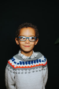 Smiling boy looking away while standing against black background