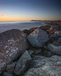 Rocks on shore against sky during sunset