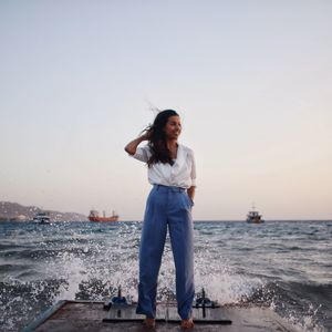 Young woman standing by sea against clear sky