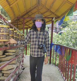 A long haired young guy wearing face mask, turning buddhist prayer wheel with looking at camera 