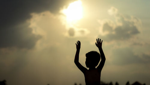 Silhouette woman with arms raised standing against sky during sunset