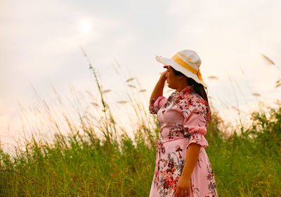 Woman wearing hat standing on field against sky during sunset