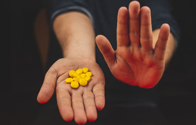Close-up of hand holding yellow flower against black background