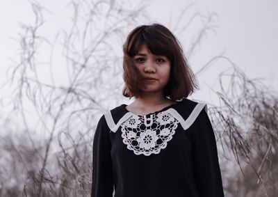 Portrait of young woman standing against bare tree