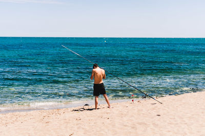 Rear view of man fishing on beach