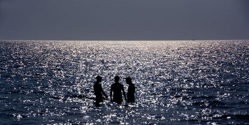 Silhouette people on sea against clear sky