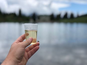 Midsection of person holding glass against lake