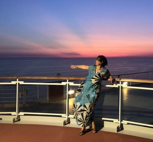 Woman standing by railing against sea during sunset