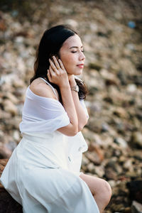 Side view of woman wearing white dress sitting on rock