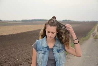 Young woman with hand in hair against farm landscape against sky