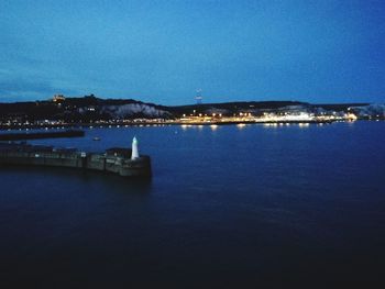 Illuminated city by sea against sky at night