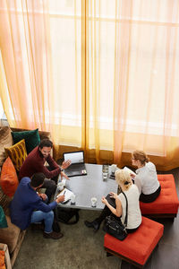 High angle view of male and female entrepreneurs discussing while sitting by table in office workshop