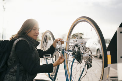 Young woman with bicycle standing against the sky