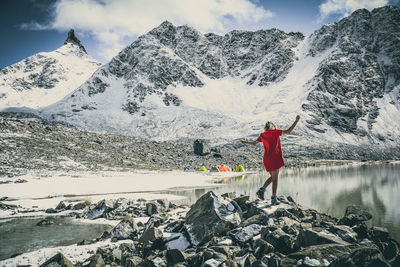 Rear view of woman standing against snowcapped mountains on rock