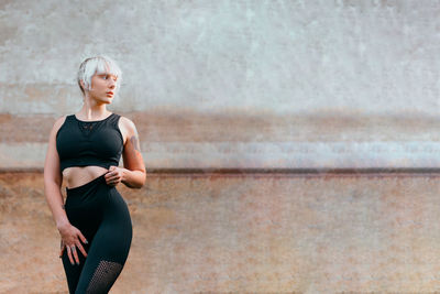 Young woman looking away while standing against wall