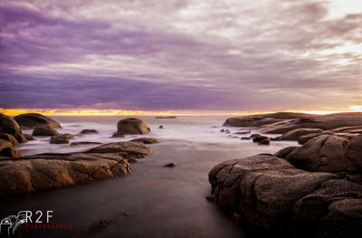 Rocks on beach against sky during sunset