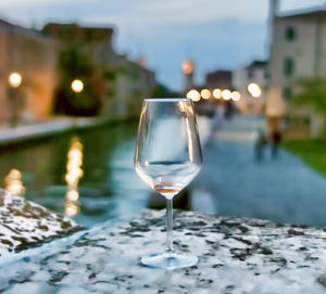 Empty wineglass on retaining wall by canal in city at dusk