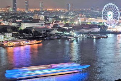 Illuminated ferris wheel by river in city at night