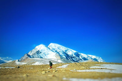 Person by snowcapped mountains against clear blue sky