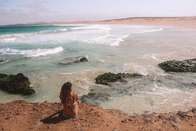 Rear view of woman wearing bikini sitting at beach