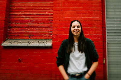 Portrait of smiling young woman standing against red wall