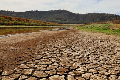 Surface level of dirt road amidst land against sky