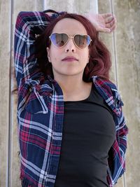 Portrait of woman wearing sunglasses lying on bench outdoors