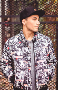 Man wearing cap and jacket while standing against fence