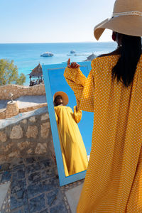 Beautiful african american woman in bright yellow dress admires in mirror on vacation by sea