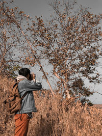Rear view of man photographing tree against sky