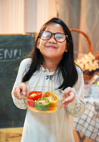 Portrait of smiling girl holding bell peppers in bowl at restaurant