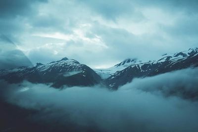 Snowcapped mountains against cloudy sky seen through airplane window