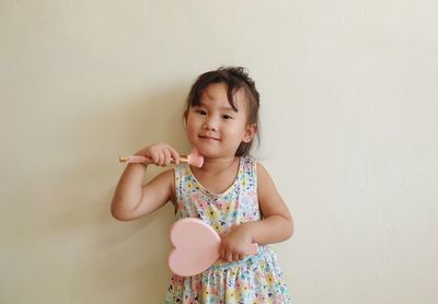 Portrait of smiling girl applying make-up while holding mirror against wall